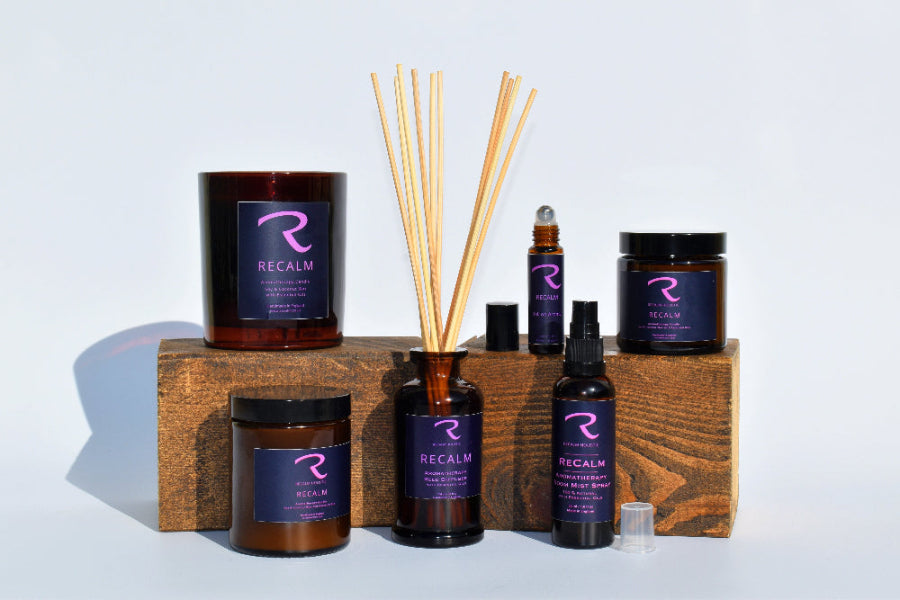 Collection of ReCalm products including candles, diffusers, and bottles on a wooden block with a white background.