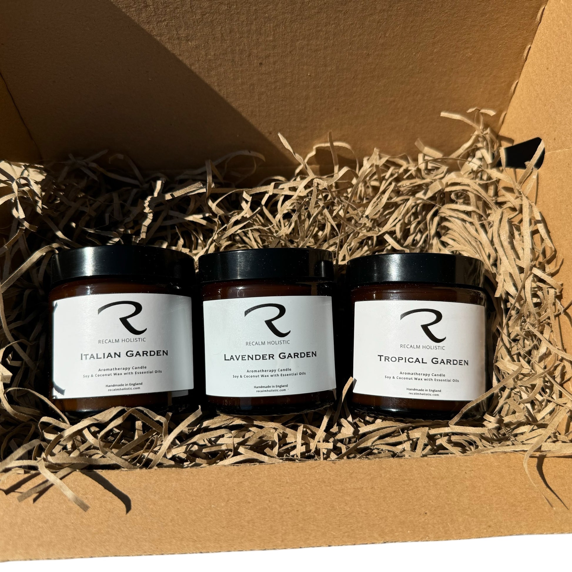 Three candles labeled 'Italian Garden', 'Lavender Garden', and 'Tropical Garden' in a cardboard box with straw padding.