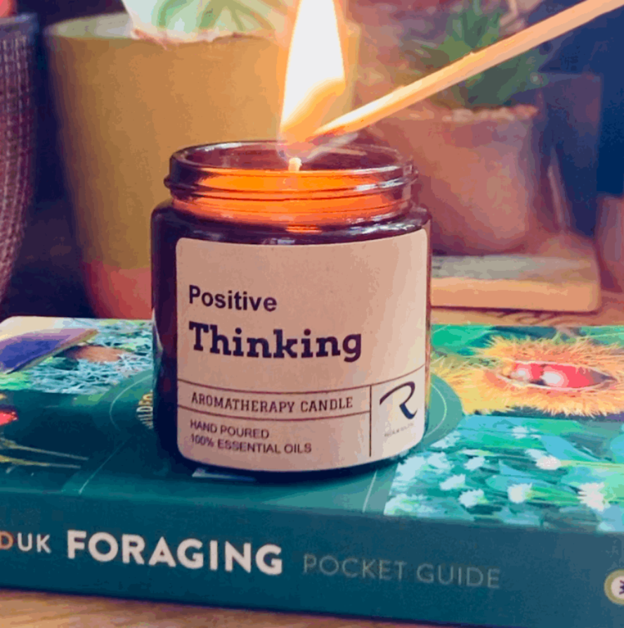 Candle labeled 'Positive Thinking' being lit on a book with plants in the background