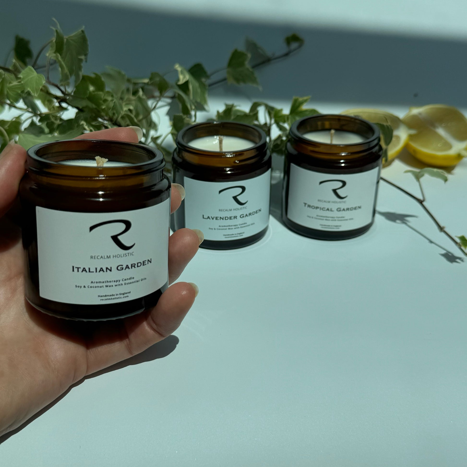 Three small jars of Ream Nourish candles with labels on a light surface, surrounded by greenery and lemons.