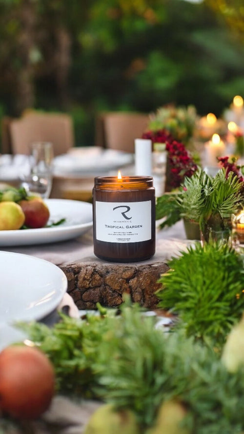 Candle with a label on a table set outdoors with fruit and plants