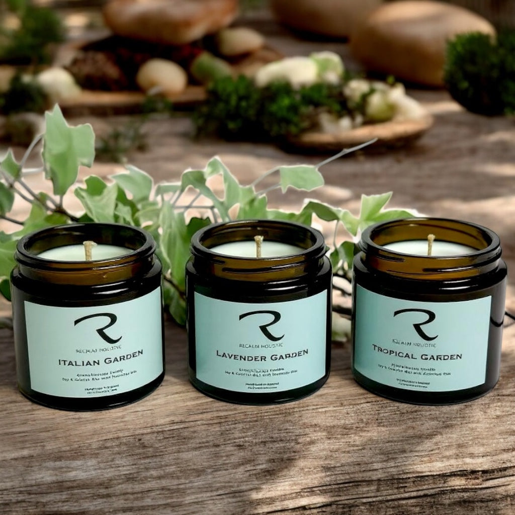 Three candles with labels on a wooden surface, surrounded by greenery Garden Candles, Italian Garden, Lavender Garden and Tropical Garden
