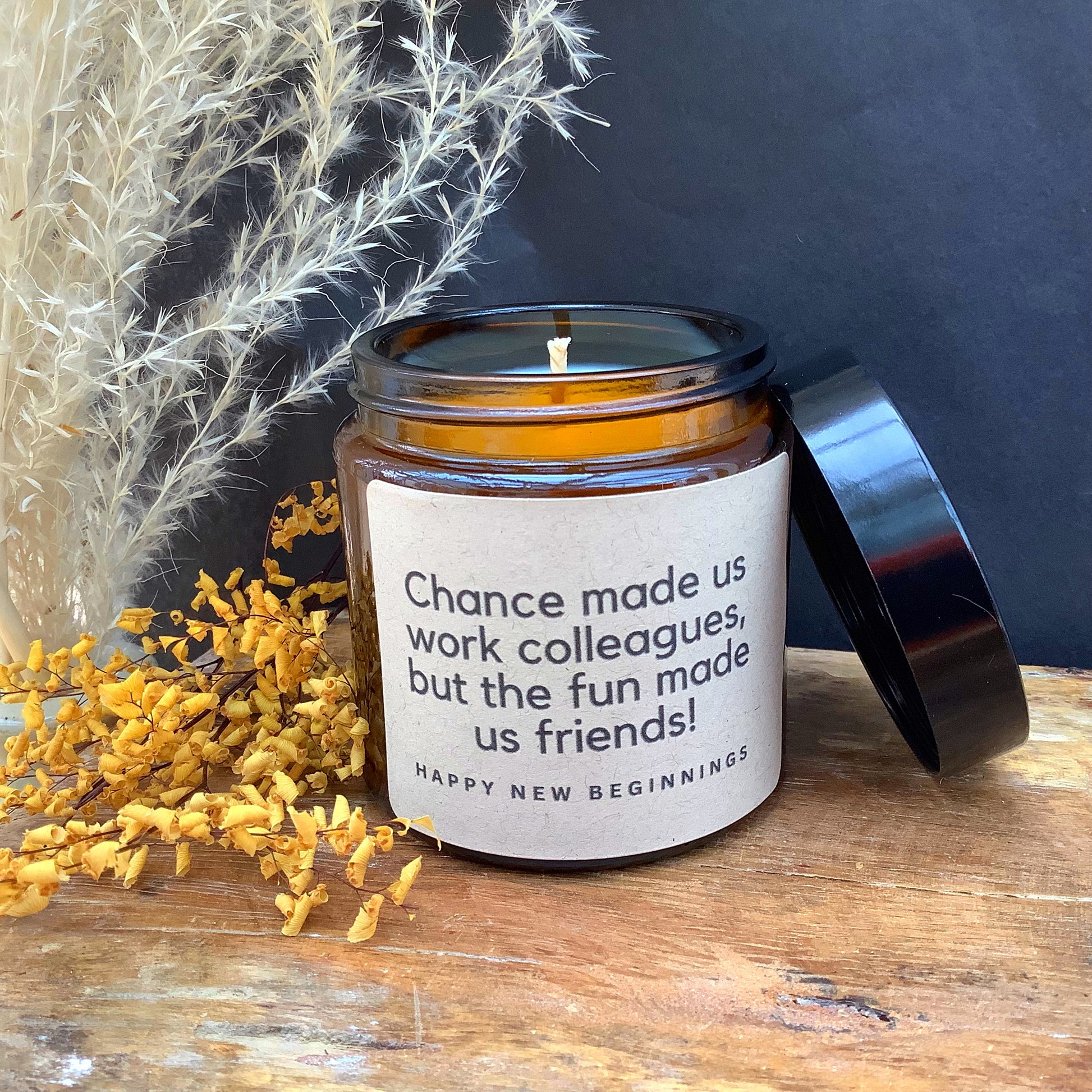 Candle in a jar with a quote on a wooden surface with dried flowers and branches.