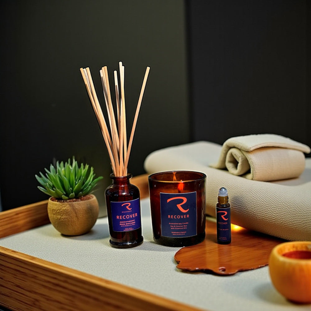 Recover diffuser, candle, and roll on aroma for pulse points with eucalyptus, rosemary and pine ssential oills, bottle on a tray with a plant and towel in the background, ritual for self care 