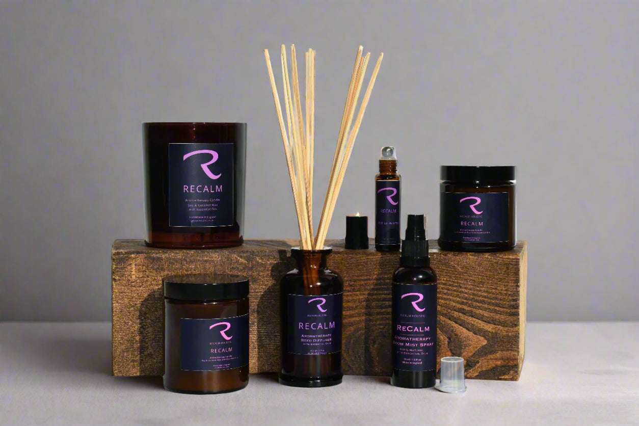Collection of Recalm Holisitc products including candles, diffusers, and roll-on remedy on a wooden block with a gray background.