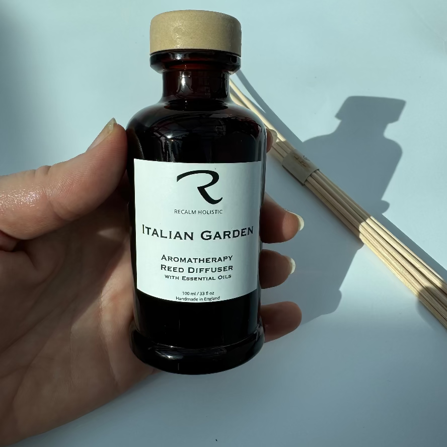 Hand holding an aromatherapy reed diffuser bottle labeled 'Italian Garden' on a light background
