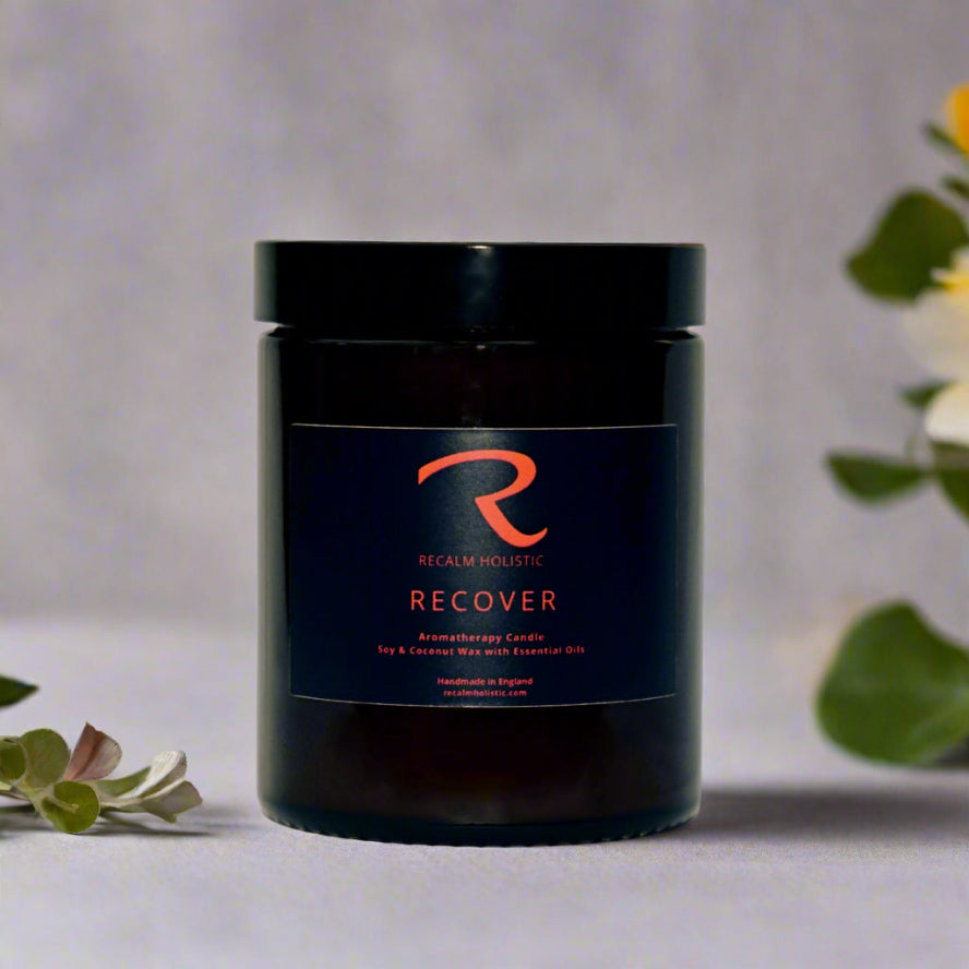 Candle jar labeled 'Recover' by Reclaim Holistic on a neutral background with greenery.