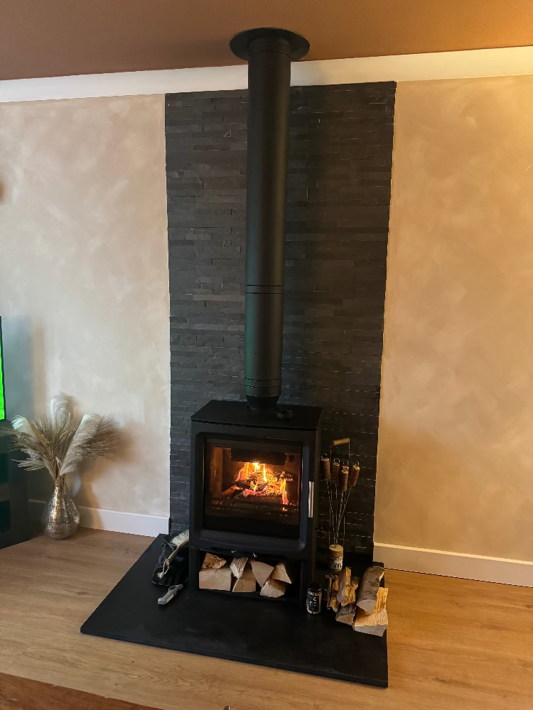 Wood-burning stove with fire lit in a room, featuring Wax Melter on top of stove and Strike a Light Matches besides it on the floor all by ReCalm Holistic. 