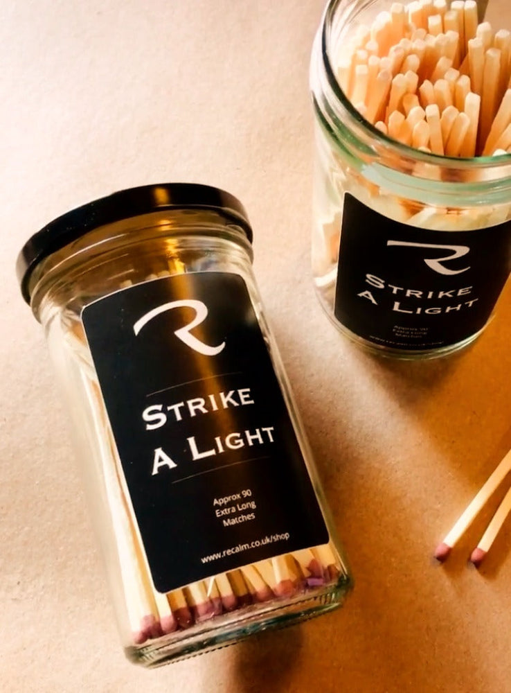 Premium brown-tipped wood matches inside a Strike a Light glass storage jar with a sleek black metal lid by ReCalm Holistic.